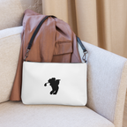 White pouch with a black silhouette of a person holding a golf club on a beige couch, with a brown leather backpack on top.