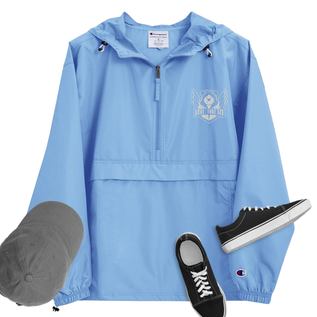 A light blue packable jacket with embroidered 'C' logo on the left sleeve, a hood, front kangaroo pocket, and a zipped pouch pocket. It is displayed alongside a grey hat and black sneakers.
