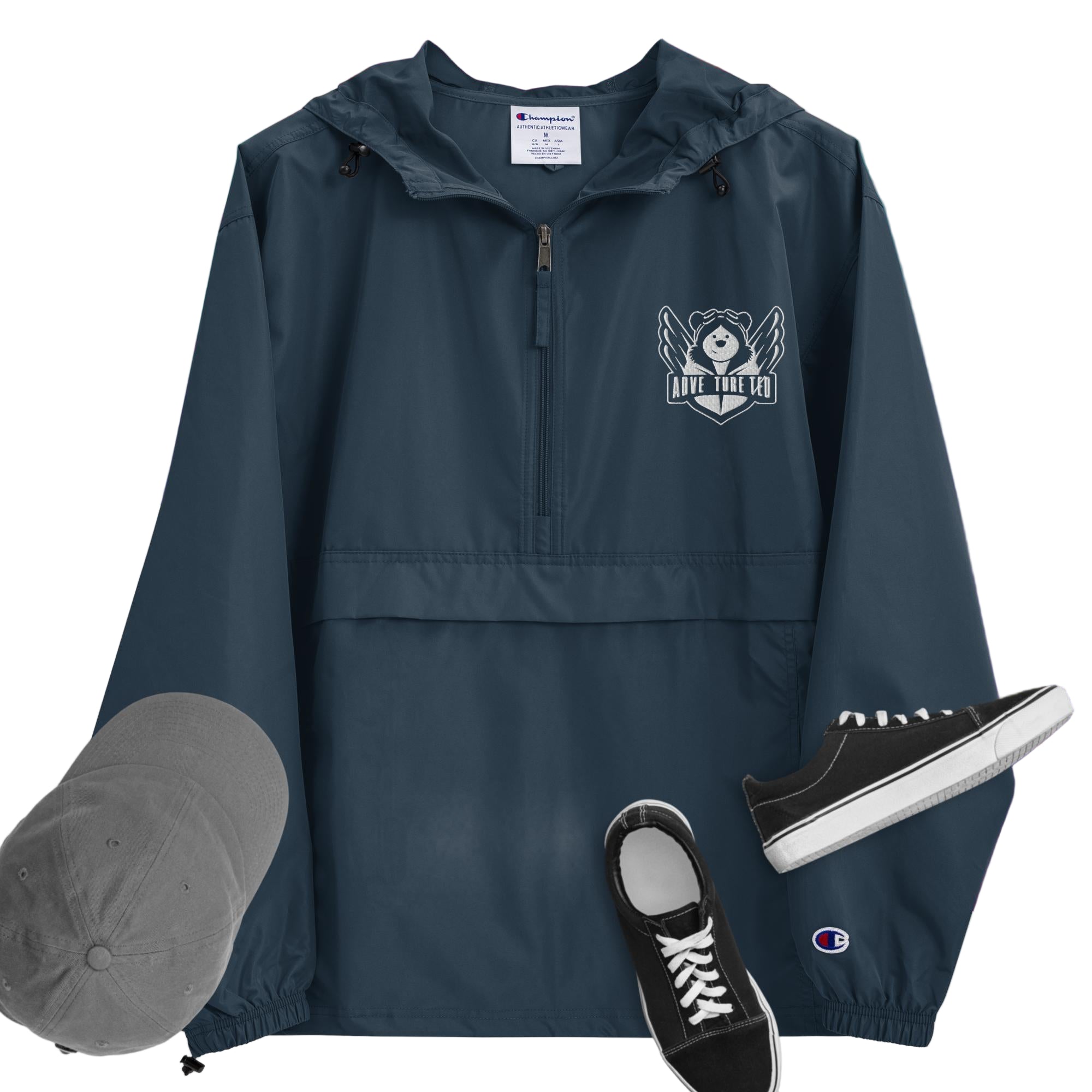 A navy packable jacket with embroidered 'C' logo on the left sleeve, a hood, front kangaroo pocket, and a zipped pouch pocket. It is displayed alongside a grey hat and black sneakers.