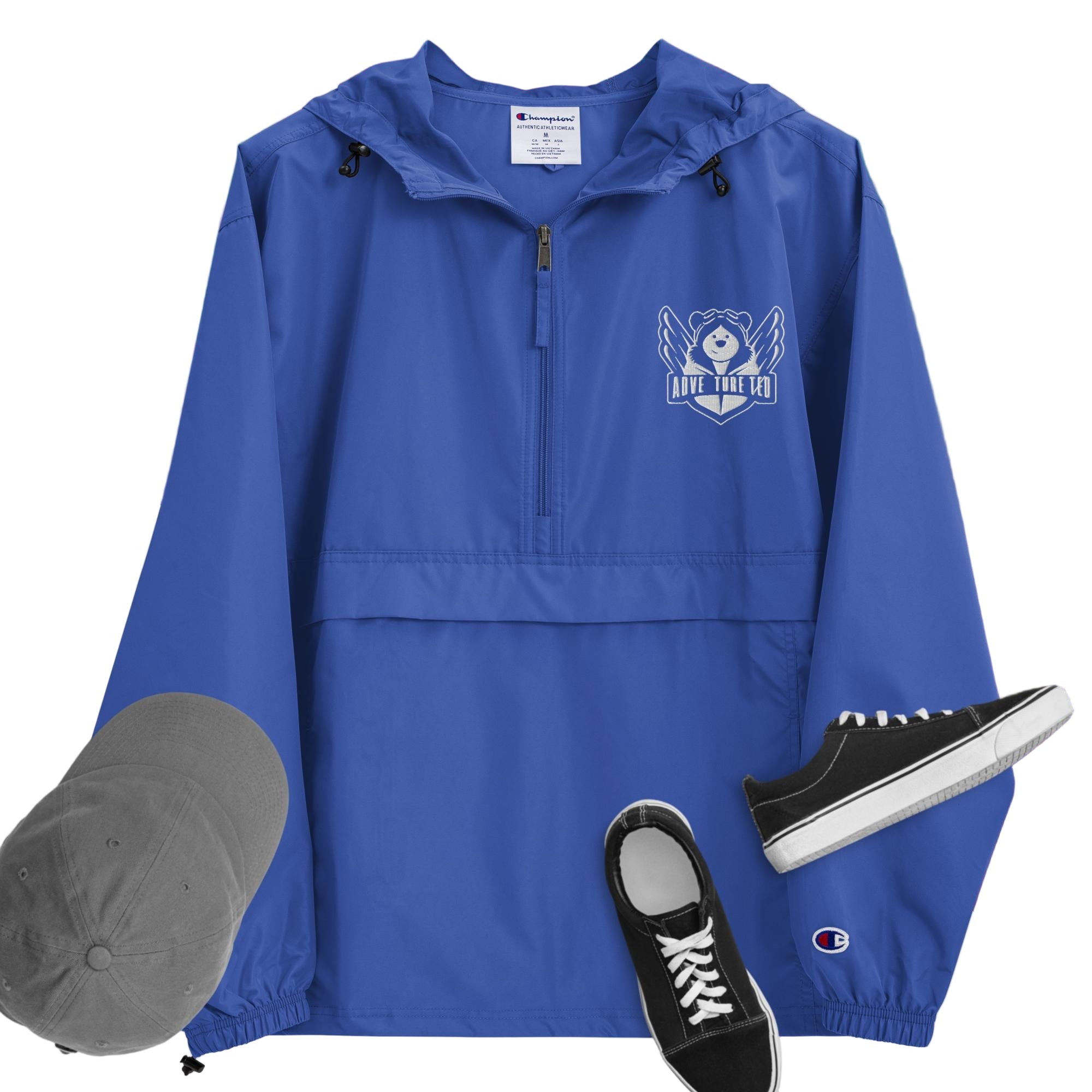 A royal blue packable jacket with embroidered 'C' logo on the left sleeve, a hood, front kangaroo pocket, and a zipped pouch pocket. It is displayed alongside a grey hat and black sneakers.